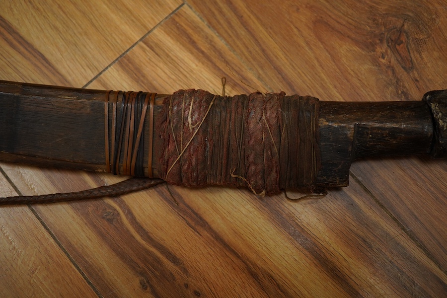 An elaborate Dayak headhunter’s sword Mandau, curved blade with chiselled and engraved back edge, large bone grip carved with protruding teeth, etc. in its wooden scabbard. Condition - good, some age wear.